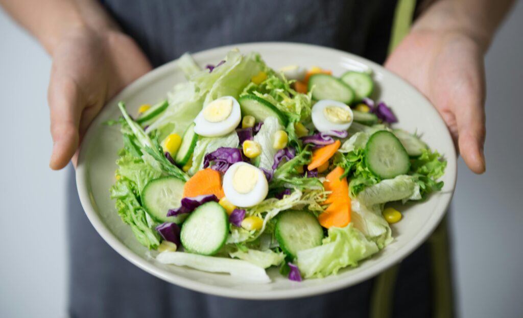 A plate of salad featuring leafy greens, eggs, carrots, and cucumber.
