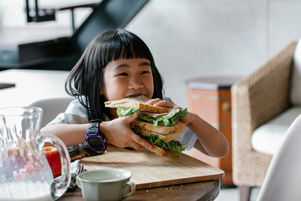 A happy child takes a bite out of a huge sandwich.